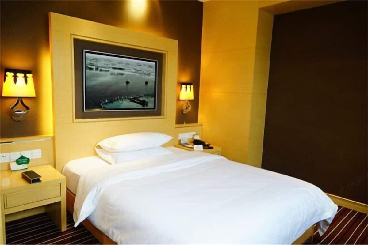 A hotel room with a bed, bedside lamps, a framed picture on the wall, and a nightstand with a phone and a green card.