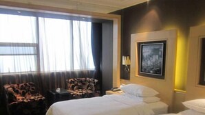 Une chambre d’hôtel avec deux lits, une chaise, une table de chevet, une lampe et un tableau encadré au mur.