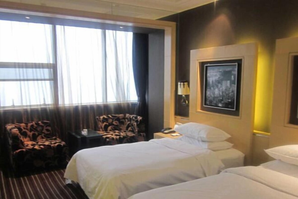 A hotel room with two beds, a chair, a bedside table, a lamp, and a framed picture on the wall.