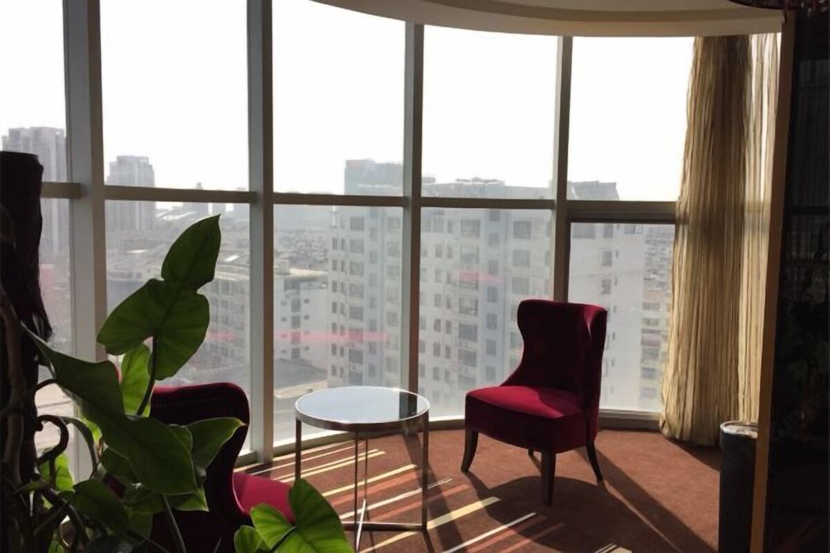 A room with large windows, a red chair, a small round table, and a potted plant.