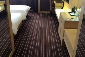 A hotel room with two beds, a desk with a lamp, and a minibar.