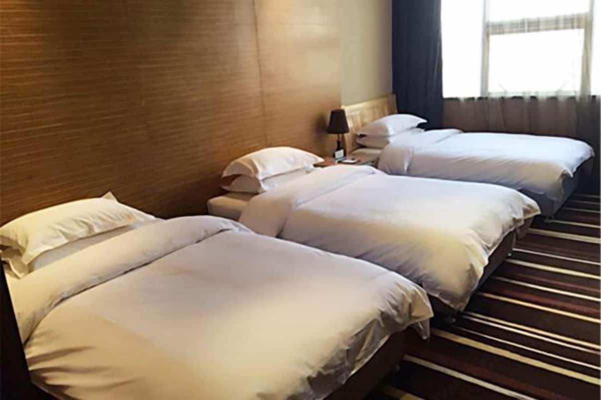 A hotel room with two beds, a nightstand, a lamp, and a window with curtains.
