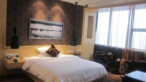 Une chambre d’hôtel avec un grand lit, un tableau au mur, une table de chevet, une lampe et une fenêtre avec des rideaux.