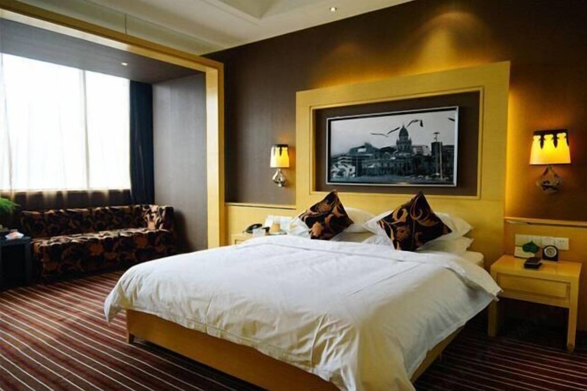 A hotel room with a large bed, a sofa, a framed cityscape picture, and two bedside lamps.