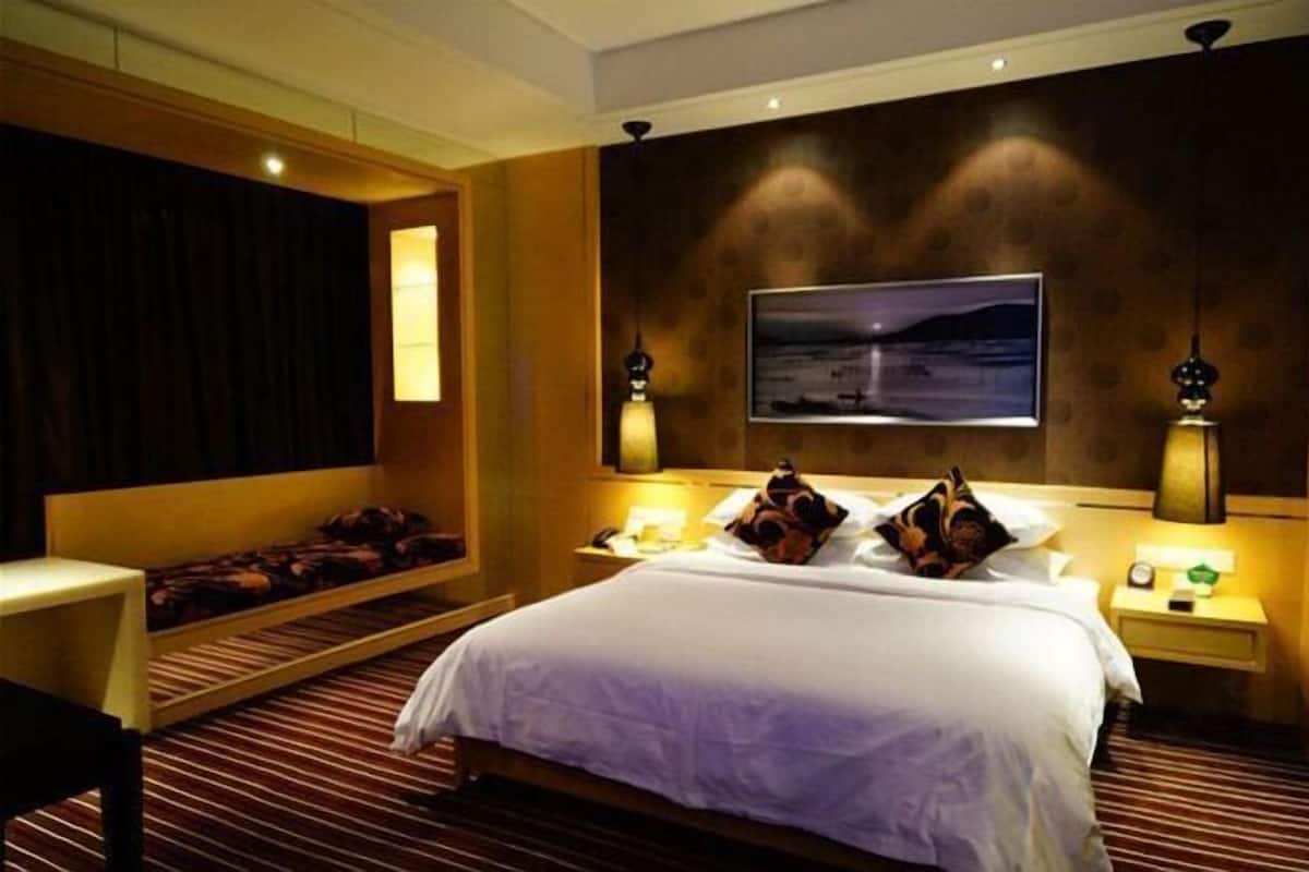 A hotel room with a large bed, a bedside table, a nightstand, a wall-mounted TV, and a window with curtains.