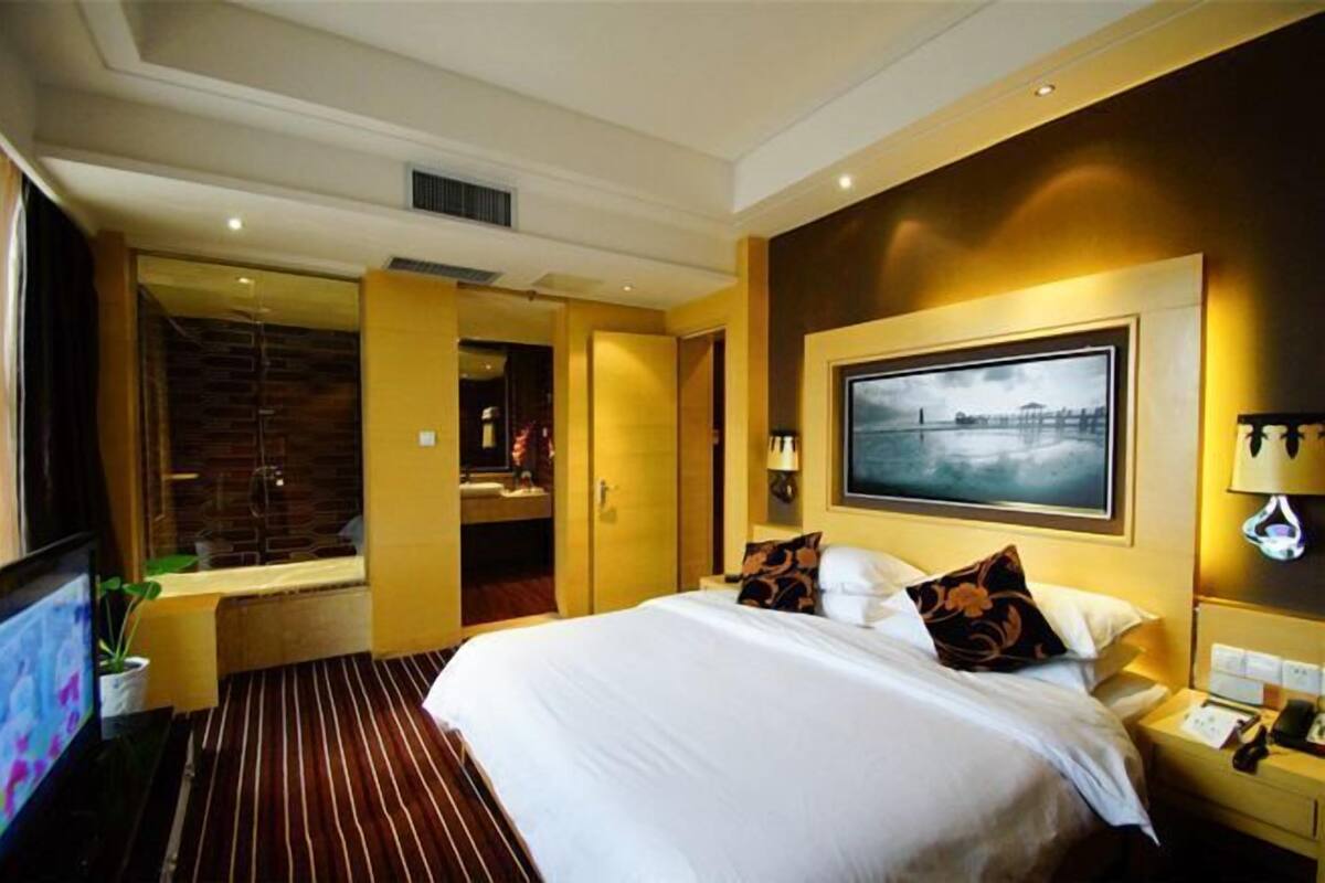 A hotel room with a large bed, a flat-screen TV, a desk with a lamp, and a large window.