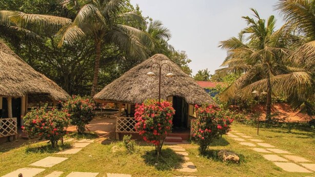 Un complexe hôtelier tropical doté de bungalows aux toits de chaume, d’un sentier dallé et d’une végétation luxuriante.