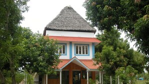 Une maison à deux étages, dotée d’un toit de chaume et entourée d’une végétation luxuriante.