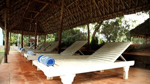 Un espace extérieur abrité, aménagé avec des chaises longues blanches et des serviettes à rayures bleues.