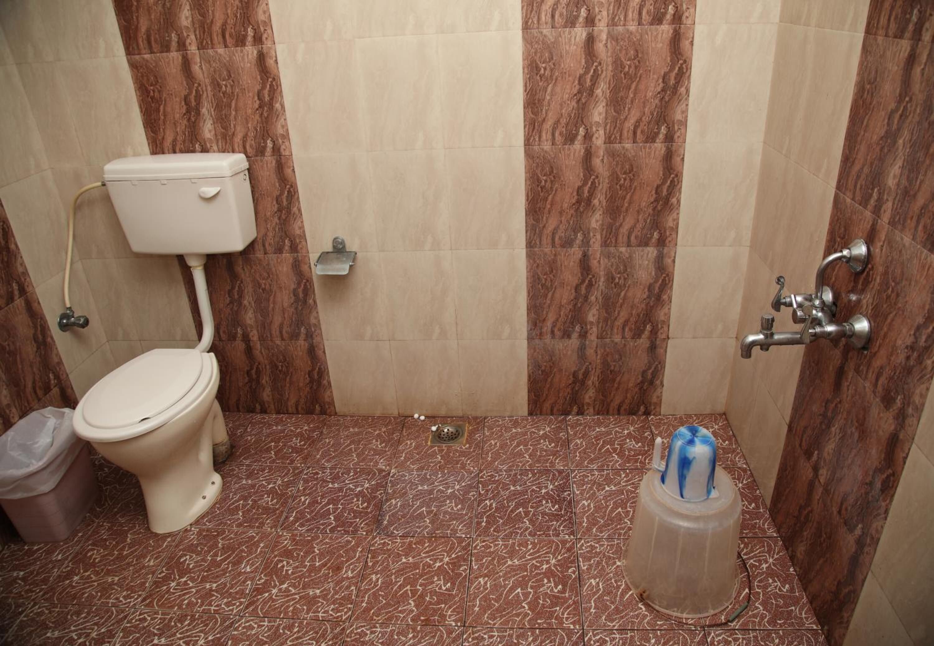A bathroom with a toilet, a trash bin, and a shower area.