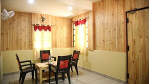 Un coin repas avec une table et des chaises en bois, un ventilateur de plafond et des murs recouverts de lambris en bois.