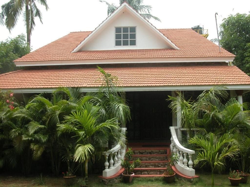 A two-story house with a red-tiled roof, a white exterior, and a front porch with a staircase.
