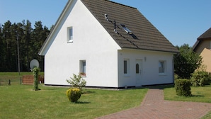 Ein eingeschossiges Haus mit geneigtem Dach, einer Satellitenschüssel und einem kleinen Garten mit einem Weg zum Eingang.