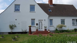 Ein zweistöckiges Haus mit einem dreieckigen Dach, einem Backstein-Schornstein und einer Haustür mit Stufen.