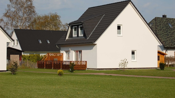 Ein modernes, zweistöckiges Haus mit Satteldach, einem kleinen Balkon und einem gepflegten Rasen.