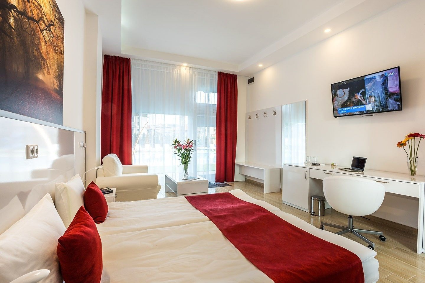 Een moderne hotelkamer met een groot bed, een bureau, een stoel, een televisie en een raam met gordijnen.