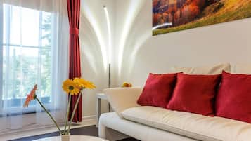 Ein modernes Wohnzimmer mit einem weißen Sofa, roten Kissen, einem Couchtisch mit gelben Blumen und einem Landschaftsbild.