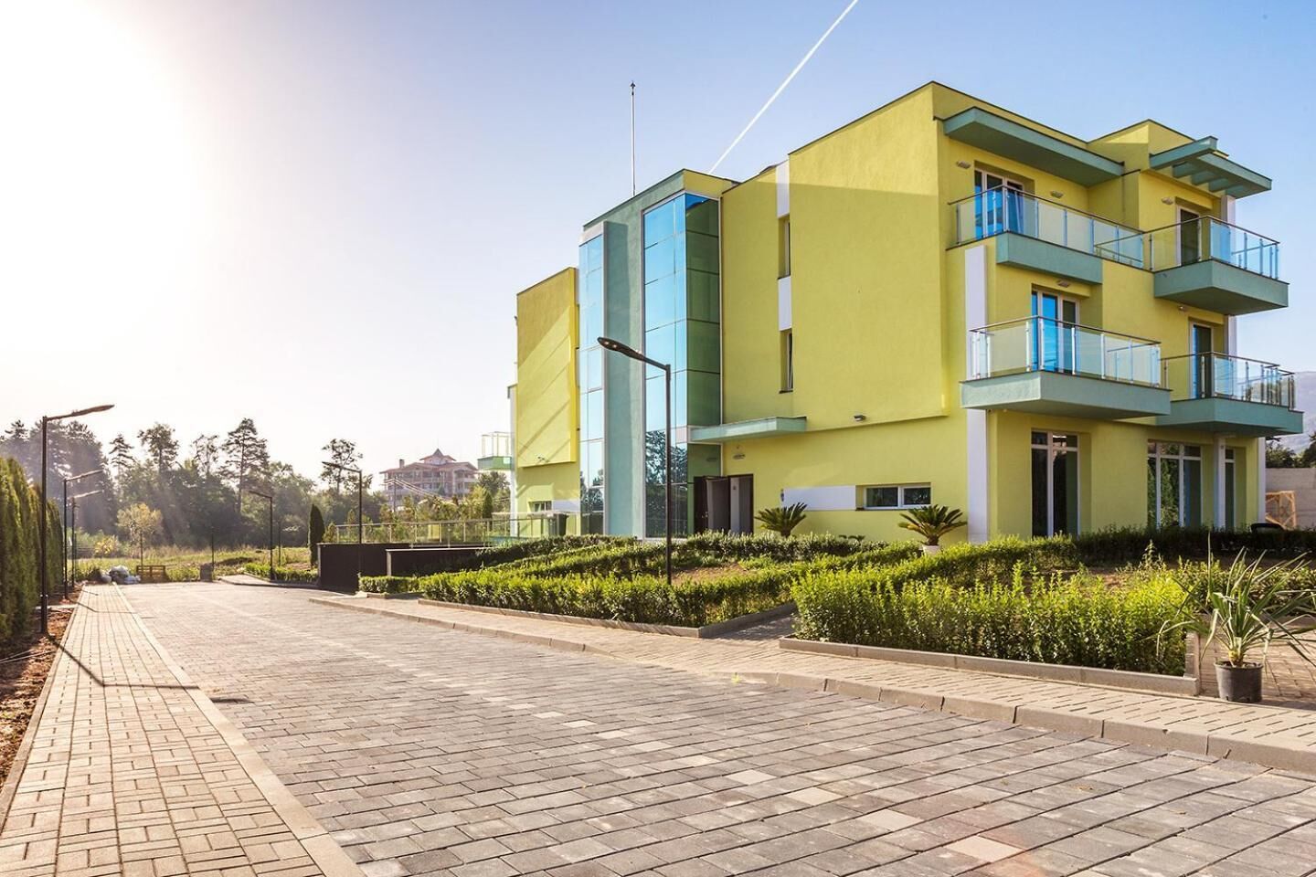 A modern yellow building with blue accents, a paved walkway, and landscaped greenery.