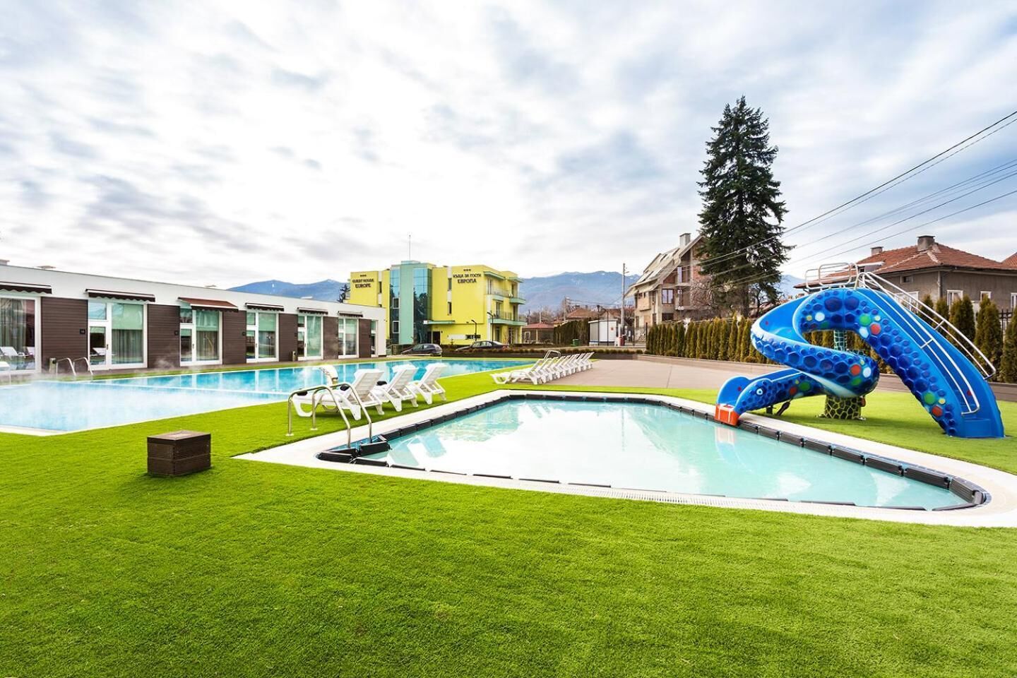 A swimming pool with a slide, lounge chairs, and a well-maintained lawn.