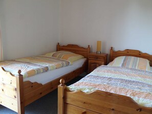 Ett sovrum med två sängar i trä, var och en med en trägavel och en träfotgavel, och ett nattduksbord med en lampa placerat mellan dem.