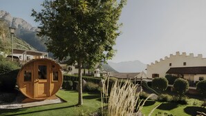 Une cabane en bois avec une porte, entourée d’une pelouse bien entretenue, de buissons et d’un arbre.