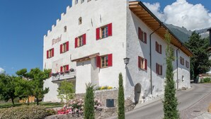 Un bâtiment blanc avec des volets rouges, un balcon et une chaîne de montagnes en arrière-plan.