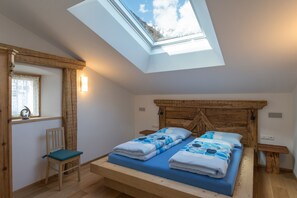 A bedroom with a skylight, a bed with blue bedding, a wooden headboard, a chair, and a bedside table. - Historic Charm Meets Modern Comfort: Sauna, Mountain Views & Terrace. Pets Welcome! (PARTSCHINS)