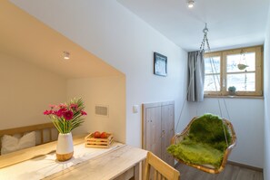 A room with a wooden table, a hanging chair, a window with curtains, and a radiator. - Historic Charm Meets Modern Comfort: Sauna, Mountain Views & Terrace. Pets Welcome! (PARTSCHINS)