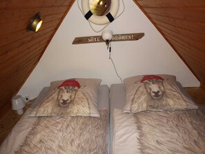 Quarto com duas camas, cada uma com um travesseiro de ovelha e uma placa acima com a inscrição 'SÖTE DRÖMEN!'.