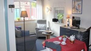 Ett mysigt rum med ett matbord dukat för två personer, en soffa, en tv och ett litet bord med en lampa.
