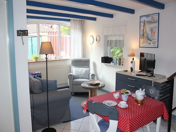 A cozy room with a dining table set for two, a sofa, a TV, and a small table with a lamp.