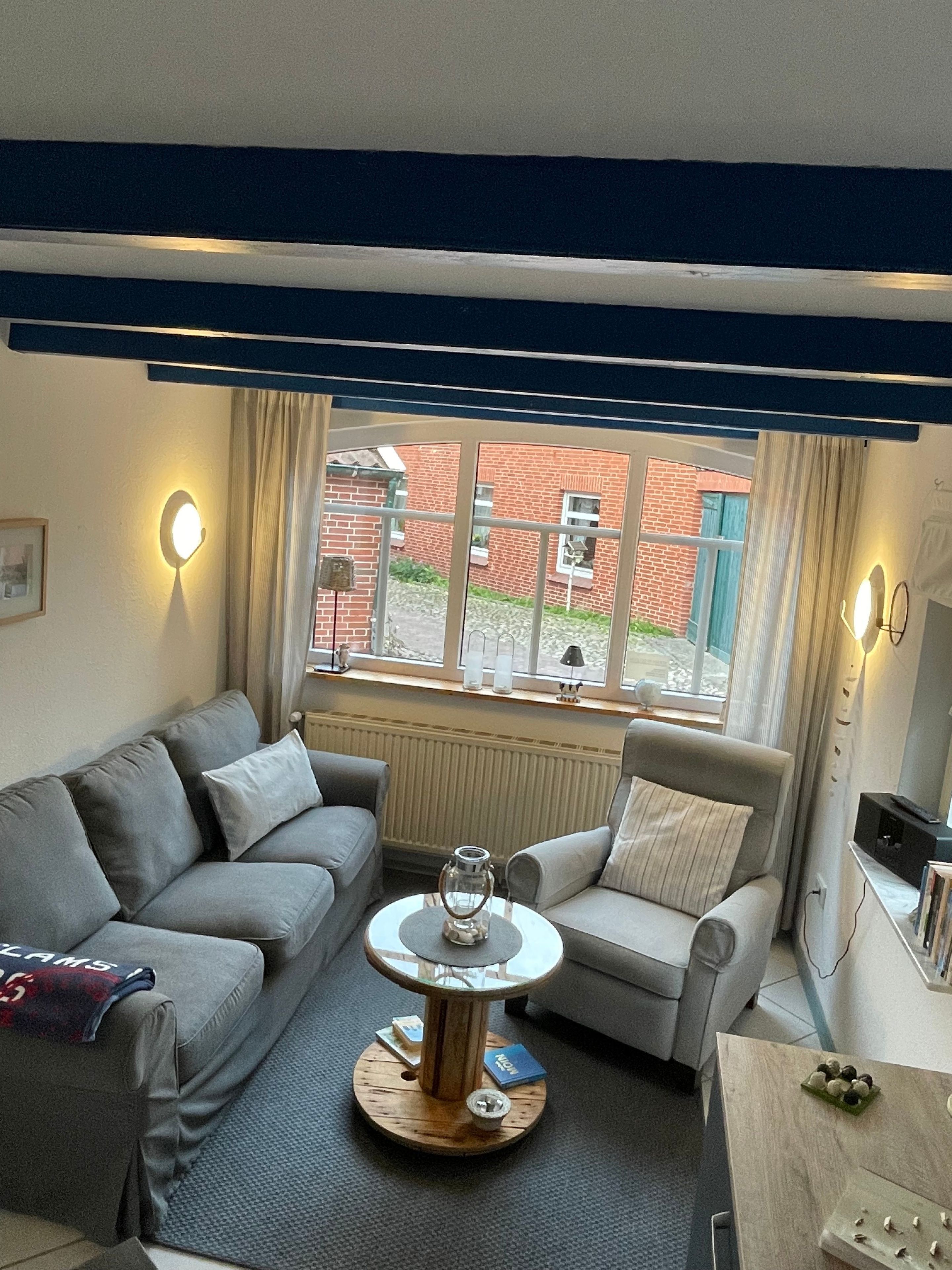 A living room with a grey sofa, a round coffee table, and a view of a brick building outside.