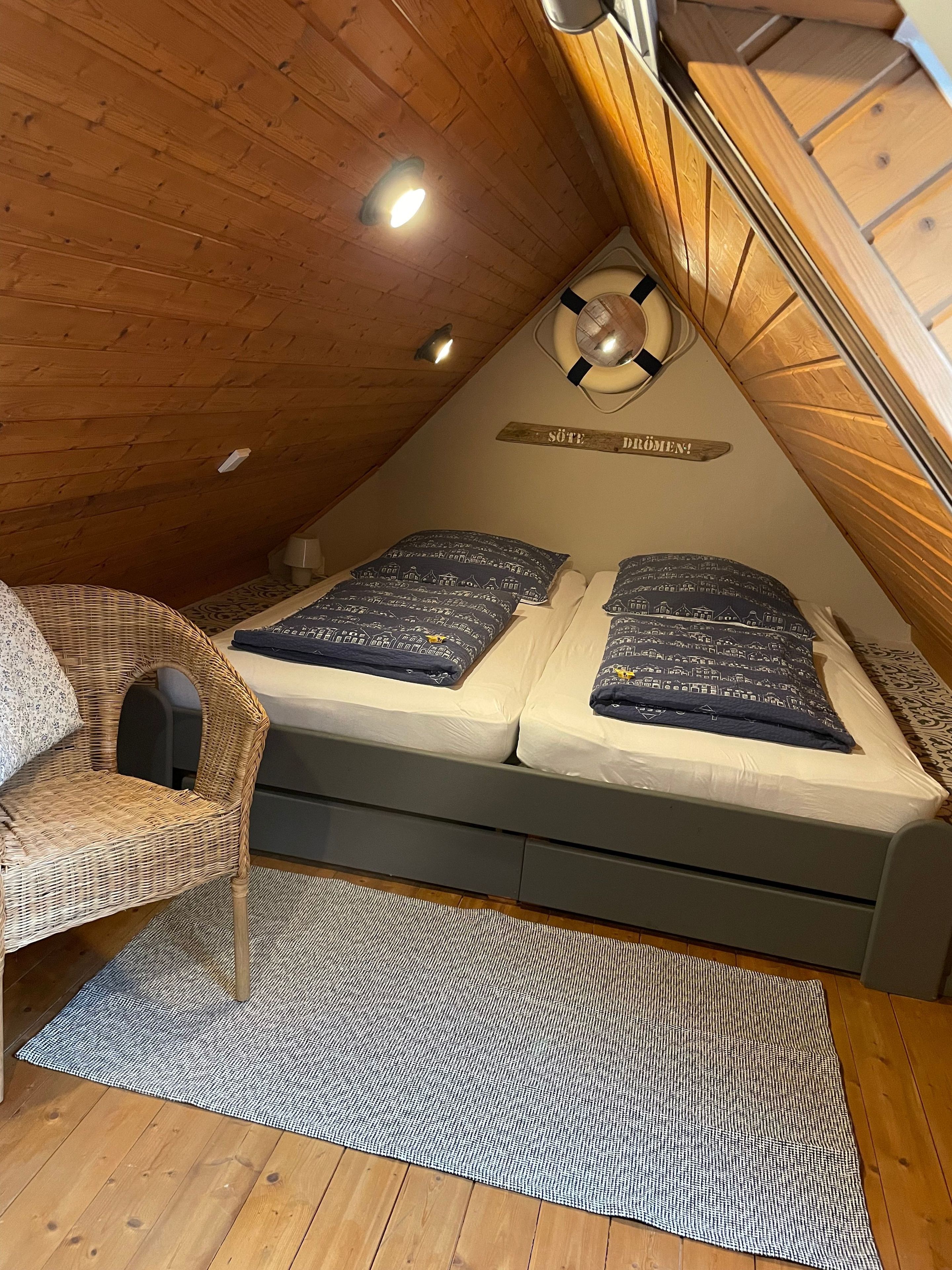 A cozy attic bedroom with a bed, a wicker chair, a small rug, and a ceiling light.