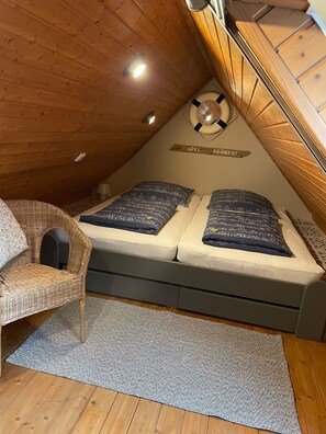 A cozy attic bedroom with a bed, a wicker chair, a small rug, and a ceiling light. - Us Huuske, 45028 - Cottage (Jemgum)