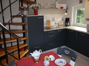 A kitchen with a wooden staircase, a dining table with a red polka dot tablecloth, and a window with a view of greenery.