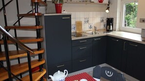 Ett kök med en trätrappa, ett matbord med en röd duk med prickar och ett fönster med utsikt över grönskan.
