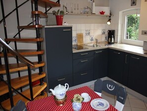 A kitchen with a wooden staircase, a dining table with a red polka dot tablecloth, and a window with a view of greenery.