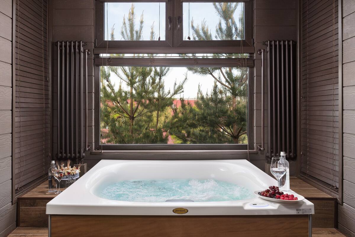 Un bain à remous avec vue sur les arbres et un bâtiment rouge à l’extérieur.