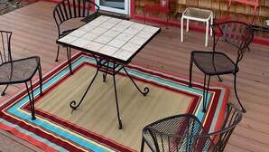 A wooden deck with a table and chairs, a door, and a window. - Wooden guest cottage (East Glacier Park Village)