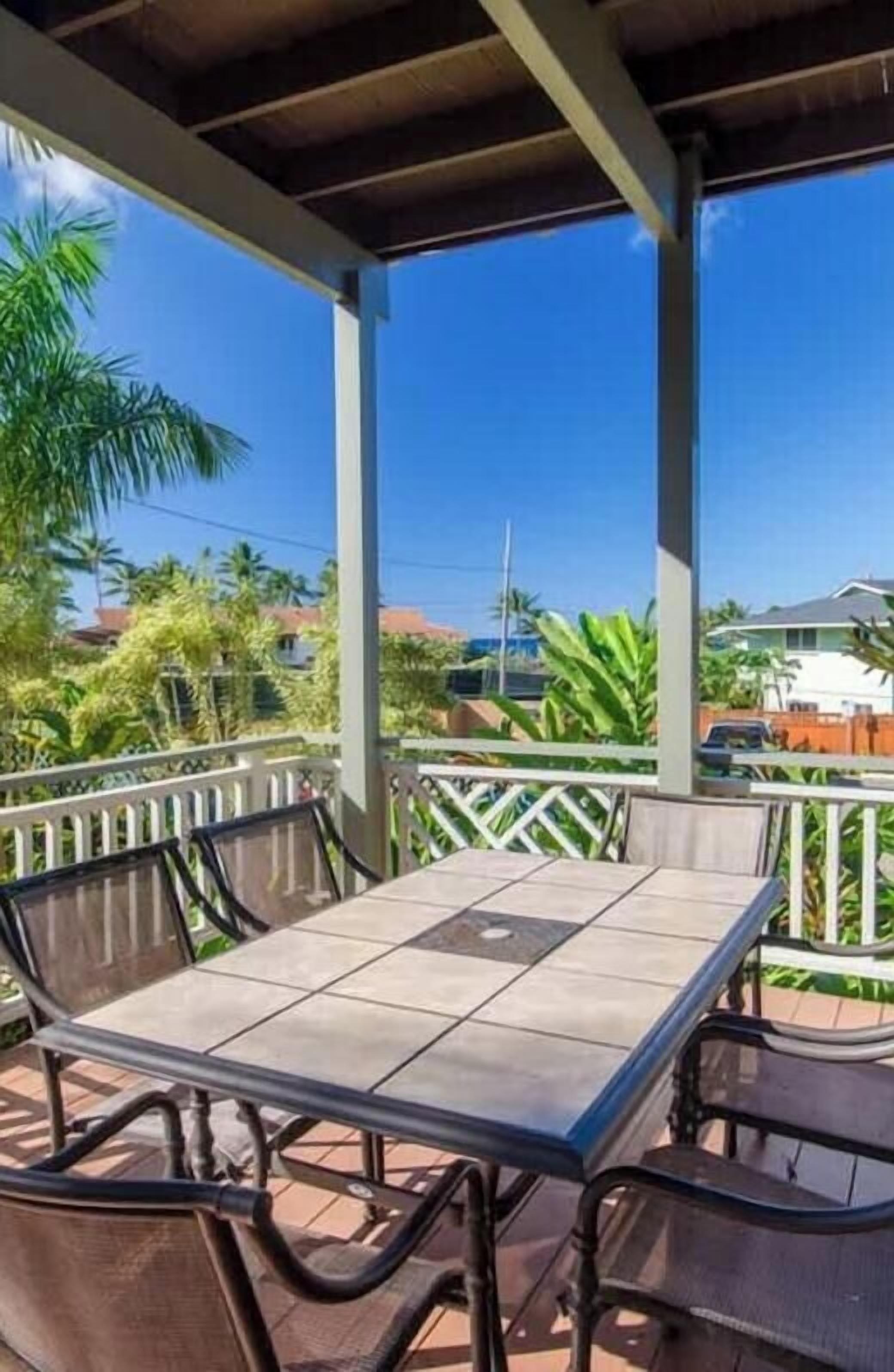A covered outdoor seating area with a table and chairs, surrounded by a railing, under a clear blue sky.