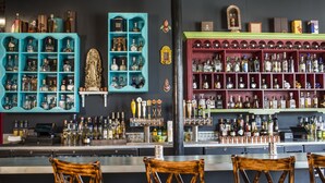 Un bar con estanterías llenas de botellas de licores, una caja registradora y sillas de madera.