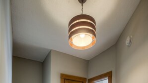 Una escalera de madera con barandilla que conduce a un segundo piso. Se ve una puerta de madera con un panel de vidrio, y una lámpara cuelga del techo.