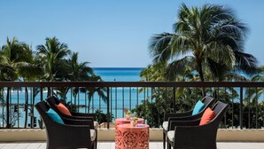 Un balcon avec deux fauteuils en osier et une petite table, donnant sur une plage bordée de palmiers et sur l’océan.