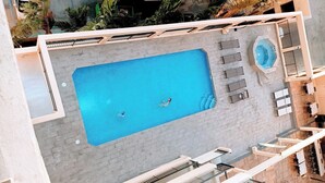 Vue aérienne d’une piscine avec deux personnes, un jacuzzi et un espace salon extérieur.