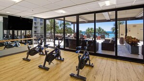 Une salle de sport équipée de vélos d’exercice et offrant une vue sur l’espace autour de la piscine.
