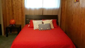 A room with a wooden wall, a bed with a red blanket, and a window with curtains. - Suite With Private Entrance 20 min to YYC Airport (Airdrie, Canada)
