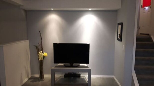 A living room with a flat-screen TV on a stand, a vase with flowers, and a staircase in the background. - Suite With Private Entrance 20 min to YYC Airport (Airdrie, Canada)