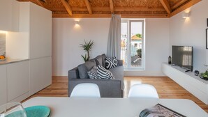 A modern living room with a grey sofa, white chairs, a TV, and a wooden ceiling. - Indulge Porto Flats (Porto)