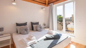 A modern bedroom with a large bed, a nightstand, a lamp, and a view of the outside balcony. - Indulge Porto Flats (Porto)