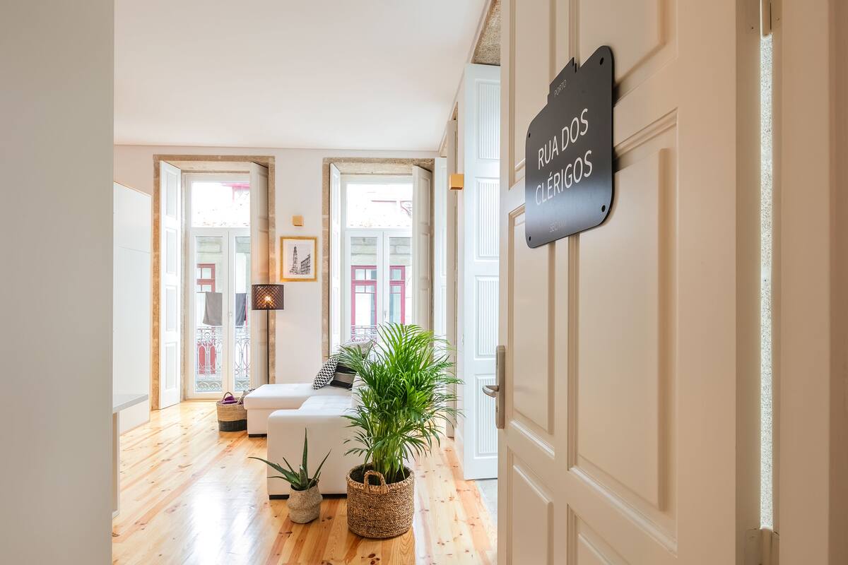 Een hal met een houten vloer, een witte bank, een potplant en een bordje met de tekst 'Rua dos Clérigos'.